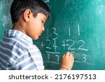 Small photo of intelligent elementary school kid solving maths problem on chalkboard at classroom -concept of talented, brilliant student and education.