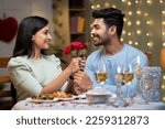 Small photo of Happy young man proposing girl by giving red roses by arranging candle light dinner - concept of love emotions, wedding present and affectionate
