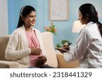 Small photo of Indian doctor or nurse counseling pregnant woman at home by writing report at home - concept of home health checkup, maternity assistance and medicare support