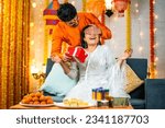 Small photo of Happy brother by closing eyes giving surprise gift to sister during raksha bandhan festival celebration at home - concept of relationship bonding, togetherness and family ceremony.