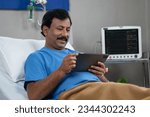 Small photo of Happy smiling indian recovered patient using digital tablet while admited on hospital bed - concept of relaxation, health recovery and technology