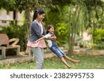 focus on mother, Cheerful indian mother playing by rotating his daughter at park - concept of weekend holidays, Carefree moments and Playful affection.