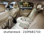 Luxury car interior made of white leather. Leather folding armrest armrest with cup holders in rear seats inside a vehicle. Clean leather interior: white rear seats, headrests and belts.