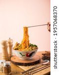 Small photo of mie ayam or chicken noodle and wooden chopsticks indonesian food with toped chicken filet and meatball on the wood table front angle with property