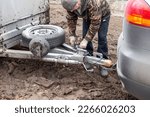 Small photo of A man checking the hitch mechanism on a car trailer in bad weather.