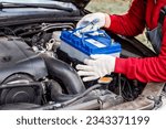 Small photo of a car mechanic installs a battery in a car. Battery replacement and repair.