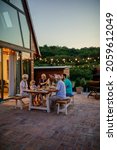 Small photo of Cheerful three generations family having dinner together around a table in the backyard. Yard is decorated with lamps