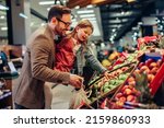 Small photo of Little girl is buying groceries in the supermarket with her father. He carrying her and picking together fresh fruits
