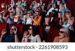 Small photo of A diverse group of people are in the movie theater watching a 3D movie. They are being frightened by a scary scene and are throwing popcorn into the air out of fear.