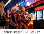 A group of diverse people are queueing up in a movie theater to watch a movie. They are holding their tickets, popcorn and drinks in their hands.