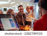 Small photo of A young joyful family is buying movie tickets at the cash register in the theater.