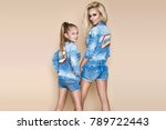 Beautiful young mother with a daughter on a beige, pastel background in studio dressed in a denim jeans clothing. Jeans fashion model. Spring fashion. Mother and daughter fashion.