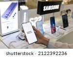 Small photo of Belgrade, Serbia - February 10, 2022: New Samsung Galaxy S22 mobile smartphone is shown in hand in electronic store. Brand logo in the background.