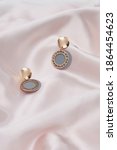 Small photo of Subject shot of two earrings with pendants. Each earring is made as curved golden disc with hanging gray plate with fretted golden rim. The pair of earrings is located on the pink silk cloth.