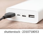 Close up of white power bank with multiple usb ports, one with plugged cable. Charging devices with a help of power bank