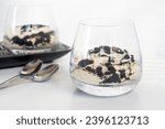 cookie and cream cheesecake in a short glass with spoon on white table.
