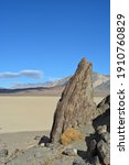 Small photo of The Grandstand on the Racetrack Playa in the Death Valley National Park, a very dark grey rock surrounded by featureless, light tan-colored clay sediment in a dry lakebed