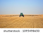 Saskatchewan farmer using a green tractor to spray his field for weeds and insects prior plowing the field and planting his spring crop of wheat or flax or soybeans or oats or other grains.
