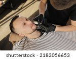 Small photo of Professional Master barber shaves the client's beard with a electric trimmer. Haircut of a man's beard in a barber shop. Barber Men. Advertising and barber shop concept
