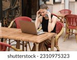 Successful young woman student, freelancer has stress with comunicating at smartphone during works remotely online on laptop on distance outdoors in cafe. Concept of remote work, digital freelance.