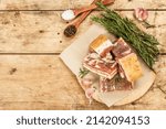 Small photo of Pieces of salty high-fat meat cooked with spices. Salo, bacon, lard, silverside, gammon. Garlic, fresh rosemary, spices. Hard light, dark shadow, wooden background, top view