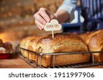 Sales Assistant In Bakery Putting Gluten Free Label Into Freshly Baked Baked Sourdough Loaves Of Bread