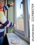 Small photo of Woman Saving Enegy Insulating Home Putting Draught Excluder Tape On Window