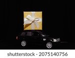 black toy car carries a gift. Gold box with ribbon. Concept of Christmas mood and preparation for the celebration. Discounts. Present. Black Friday. 2024. Seasonal sale, big discounts