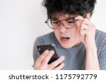 Small photo of Asian man wearing eyeglasses obsessed with his smartphone isolated on a white background. Cause of nomophobia, shortsighted, nearsighted, longsighted, farsighted, astigmatic and other eye problem.