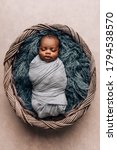 Small photo of sleepy swaddled African-American newborn baby boy laying on a blue rug in a basket with copy space