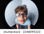 An exaggerated close up portrait of a funny little boy with glasses making a thinking face taken with a fish eye lens.