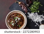 A bowl of slow cooked and braised birria beef meat in a vintage bowl with chopped onions, cilantro, guajillo peppers, and broth.