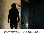A horror concept. Of a hooded figure with no face standing in the doorway of a decaying room in an abandoned ruined house
