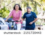Small photo of Happy Indian Senior couple riding bicycle in the park summer, active old age people and lifestyle. Elderly woman learn to ride cycle with man. retired people having enjoy life. selective focus. summer