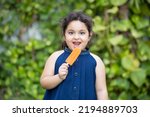 Happy cute little indian girl child enjoying ice lolly or ice cream at park.