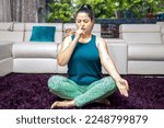 Small photo of Young indian woman in sportswear sitting in Sukhasana pose, Alternate Nostril Breathin exercise at at home. Asian Urban Female doing yoga pranayama. Full length shot.