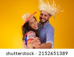 Brazilian couple wearing traditional clothes for Festa Junina dancing on yellow background