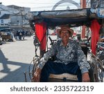 Small photo of Bandung, West Java, Indonesia - July 10, 2023. A smiling becak or pedicab driver in Bandung City. Becak's are common in Bandung and are one of the cheapest ways of getting around the city.