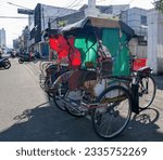 Small photo of Bandung, West Java, Indonesia - July 10, 2023. Two becak or pedicabs on a roadside in Bandung City. Becak's are used in Bandung and are one of the cheapest ways of getting around.