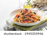 Italian lunch. Spaghetti alla puttanesca - italian pasta dish with tomatoes, olives, capers and parsley. Light background. Copy space.