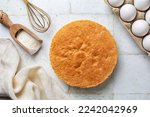 Just baked plain vanilla sponge cake on the cooking iron grid, white table, directly above. Fluffy, moist and rich chiffon Cake, two layers, homemade . Cooking utensils and ingredients on background.