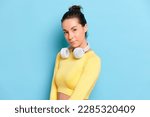 Closeup photo portrait of sporty girl model wearing yellow yoga top and white headphones on her neck, girl model posing on studio blue backdrop, natural beauty concept, copy space, high quality photo
