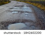 Dirty gravel road with potholes. It has some surface damage, needs maintenance, hole patching, dust binding and dragging. The cost of maintaining gravel roads, is expensive and time consuming.