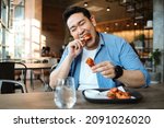 Small photo of Happy Asian man eating BBQ chicken wings in restaurant.