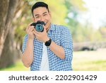 Smiling Asian man holding camera in the park,photographer with smiling face.