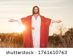 Jesus Christ with outstretched arms in welcoming blessing at sunset wearing beautiful red & white robe 