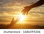 Silhouette of reaching, giving a helping hand, hope and support each other over sunset background. 