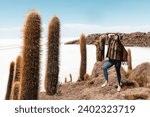 Small photo of A girl in a poncho and hat stands on a stone among large cacti. Incauasi Island, Salar de Uyuni. Bolivia