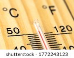 A macro shot of a classic wooden thermometer showing a temperature over 50 degrees Celsius, 122 degrees Fahrenheit.