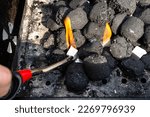 Small photo of Lighting a home grill with charcoal and white kindling for the grill, standing in the home garden, using a barbecue lighter.